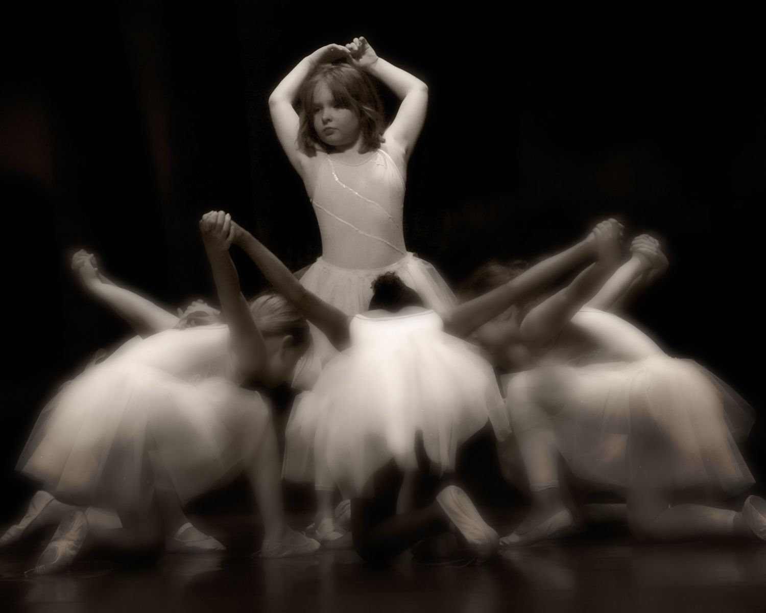 A group of young ballerinas are performing on a stage in a black and white photo.