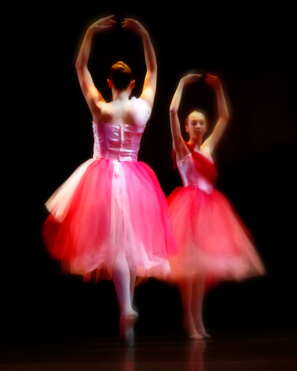 Two ballerinas in pink tutus are dancing on a stage