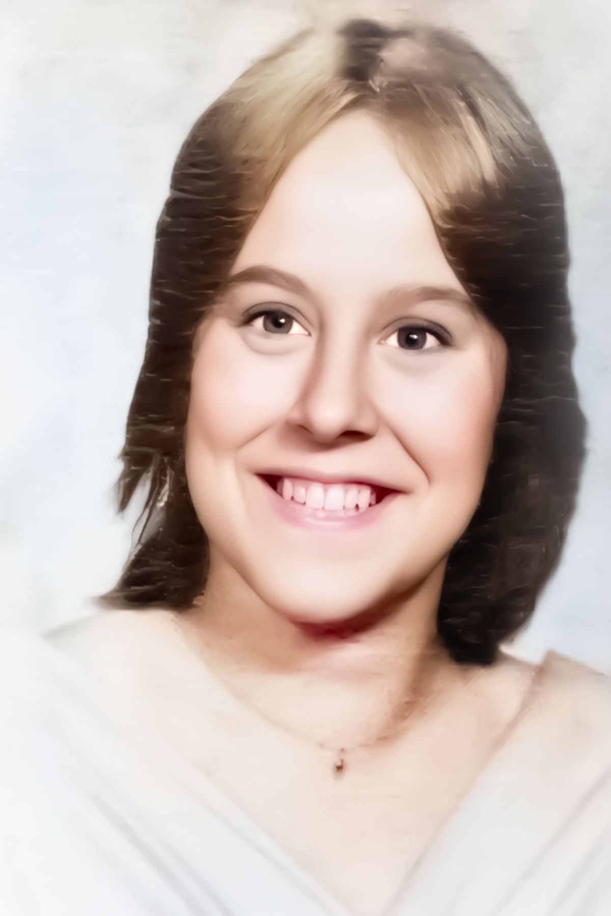 A young woman wearing a white shirt and a necklace smiles for the camera