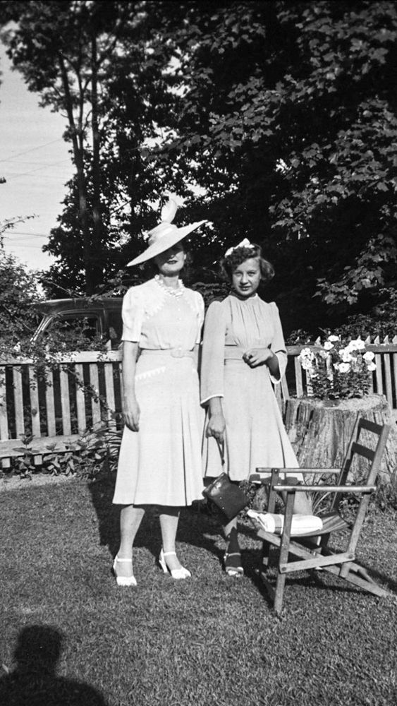 A black and white photo of two women standing next to each other in a garden.