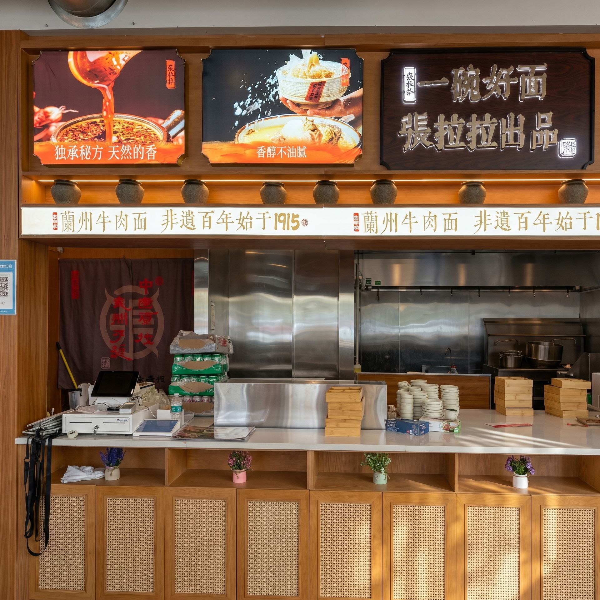 Restaurant counter with wooden decor, menu signs, and a large stainless-steel cooking area behind it.