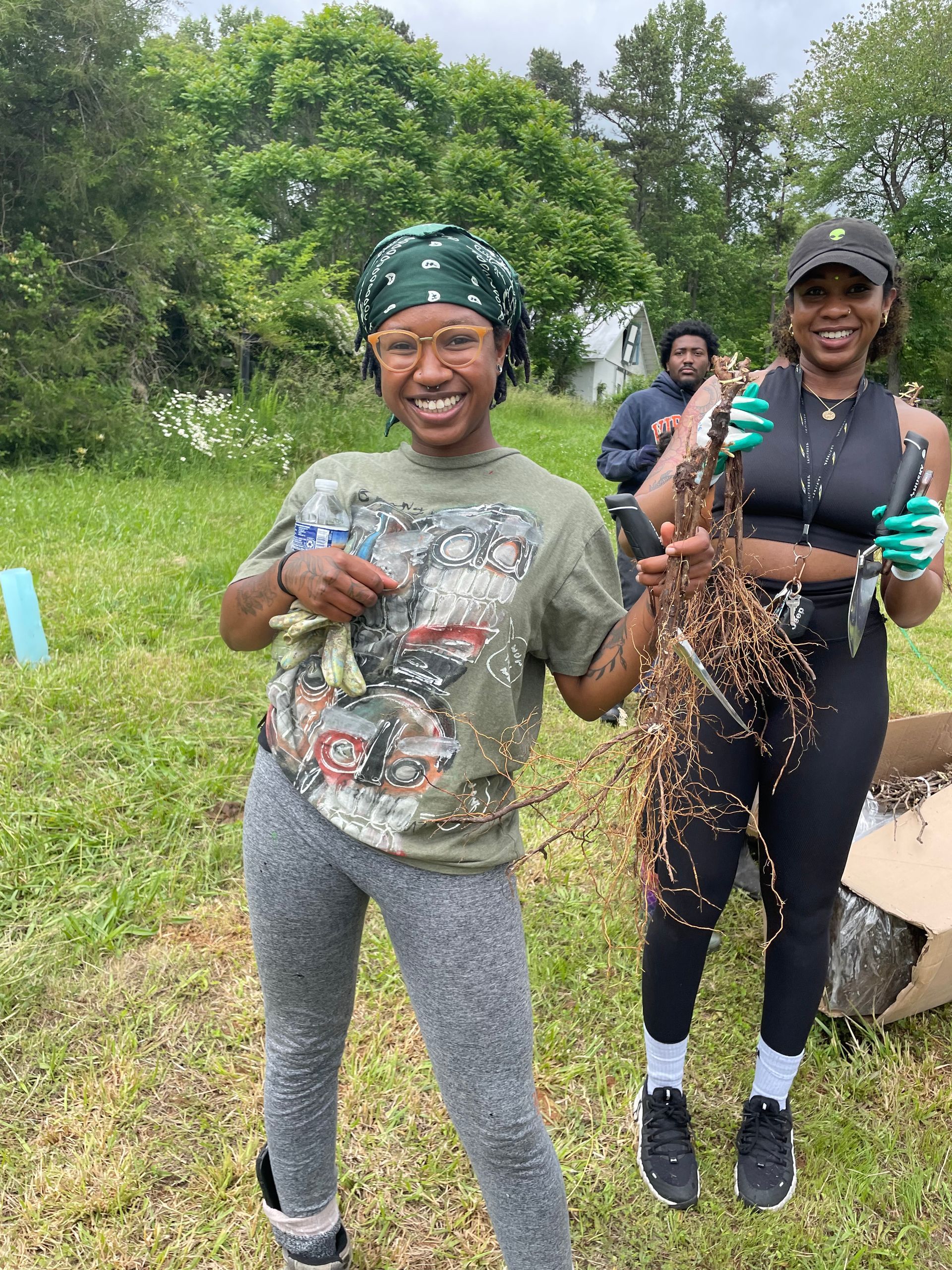 Two women are standing in a field holding roots and smiling.