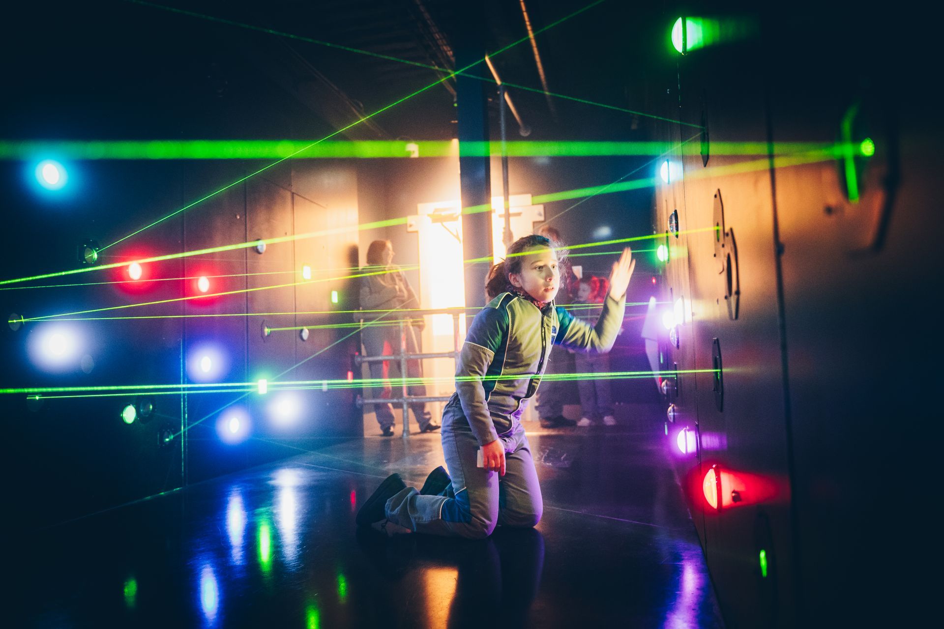 Un enfant, agenouillé, interagit avec des faisceaux laser dans un espace baigné de lumière