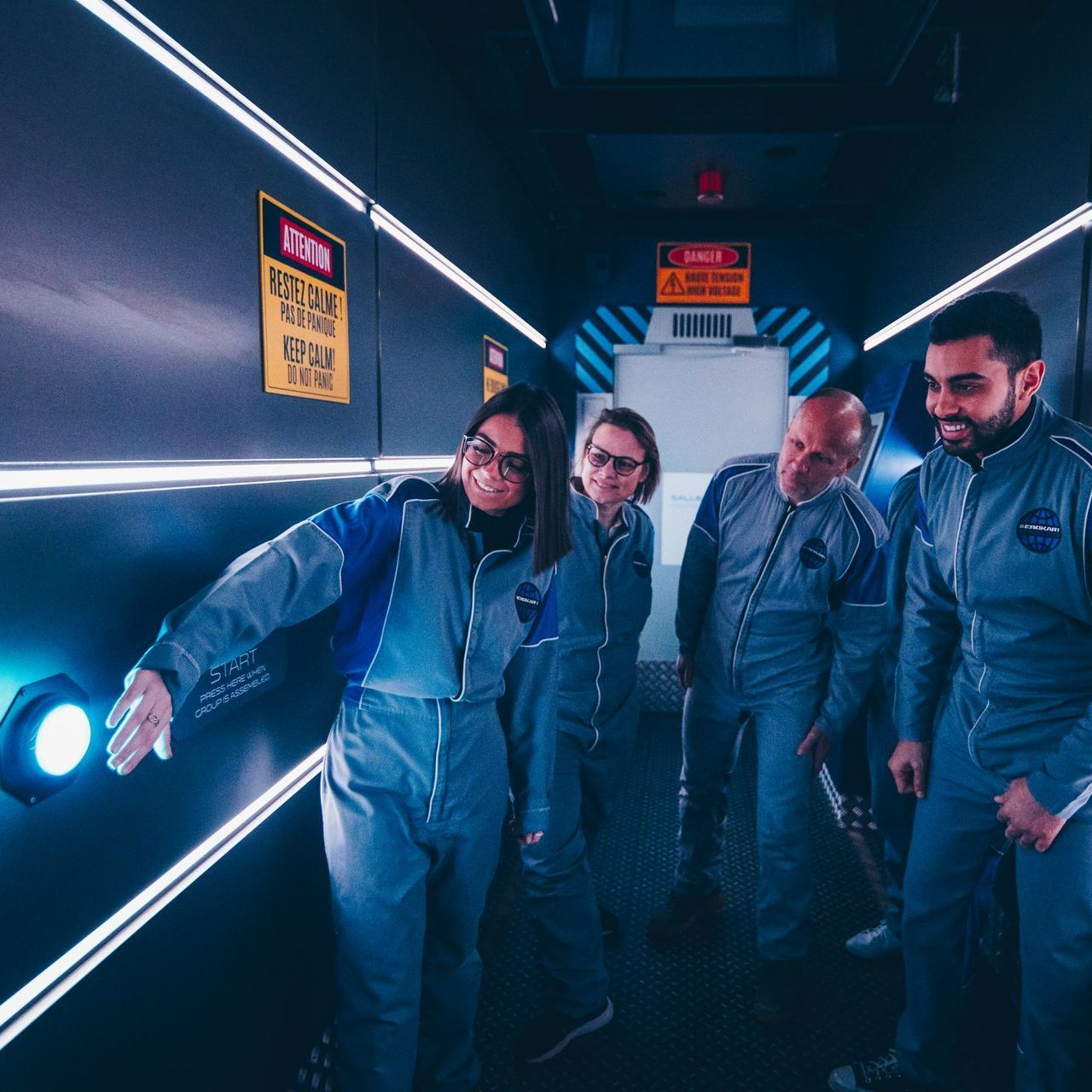 Des gens en combinaison spatiale dans un couloir futuriste ; une femme pointe du doigt une lumière bleue.