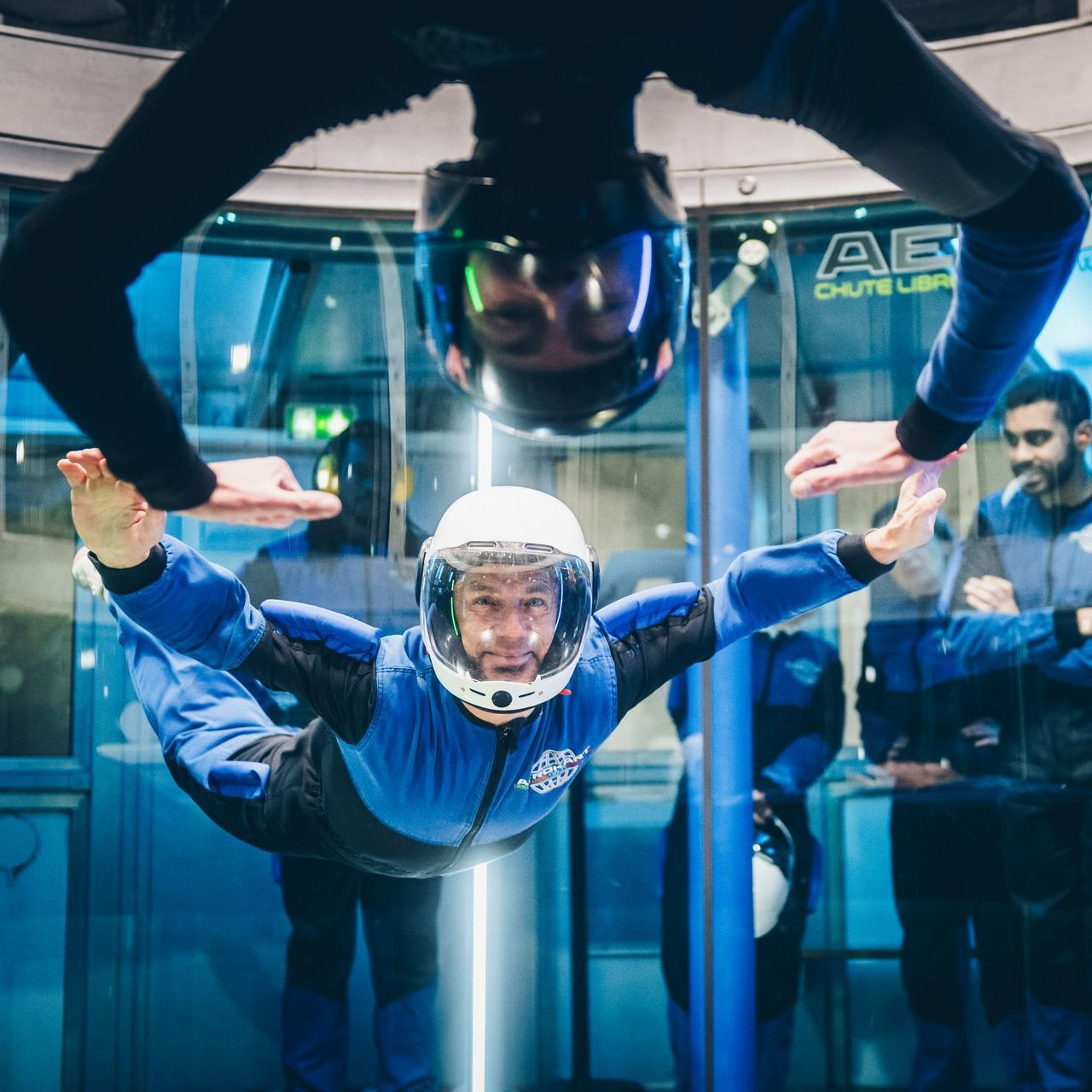 Une personne en combinaison bleue et casque flotte dans un simulateur de chute libre