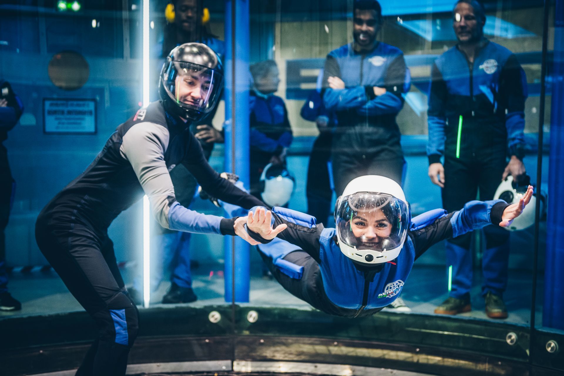Saut en soufflerie avec instructeur dans un tunnel à vent, sous le regard des spectateurs derrière une vitre.