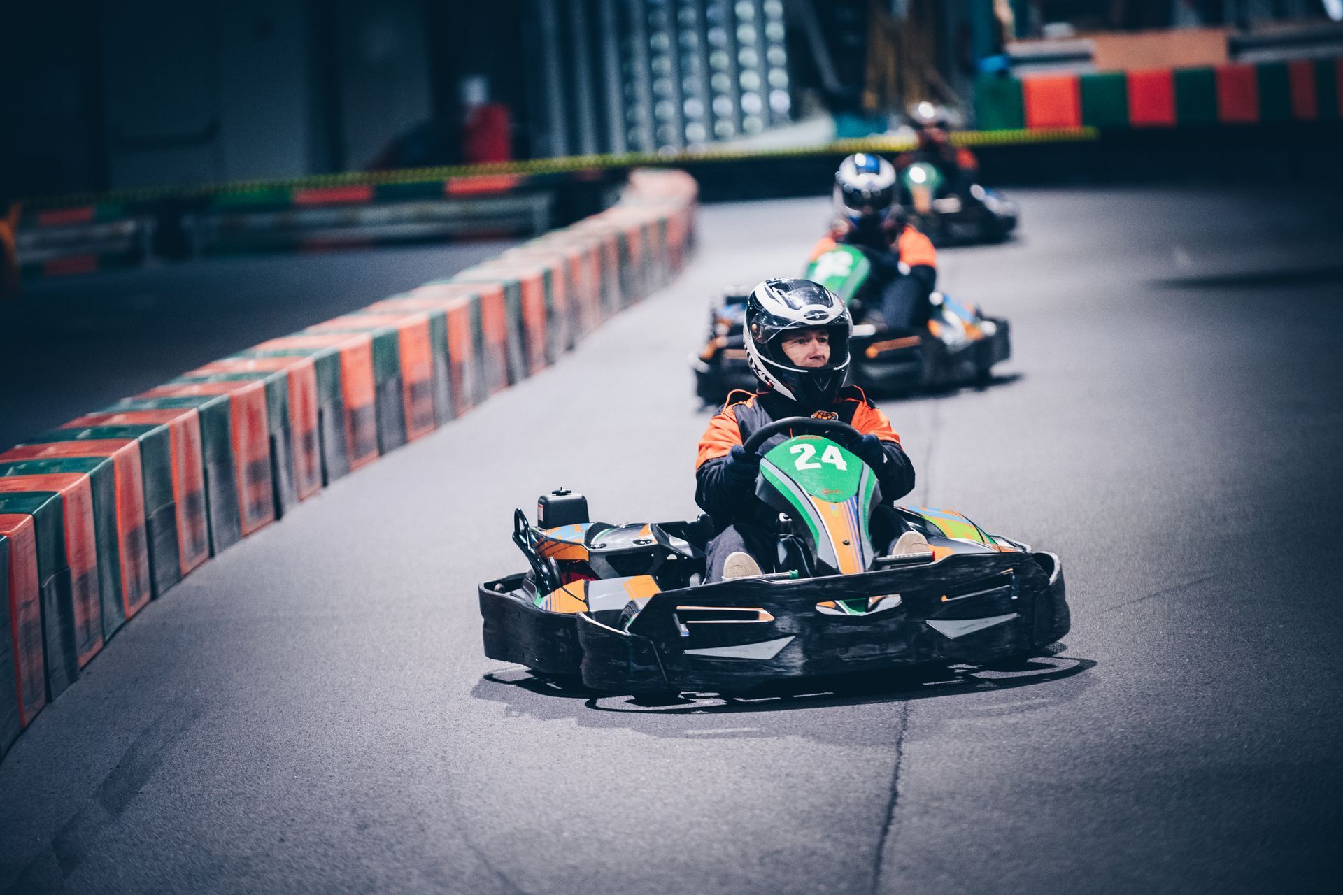 Des pilotes de karting filent à toute allure sur une piste détrempée, le kart de tête, vert et noir, aborde un virage.