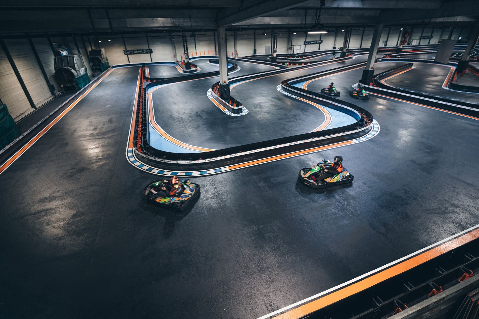 Course de karts sur une piste intérieure avec des virages serrés et des barrières colorées.