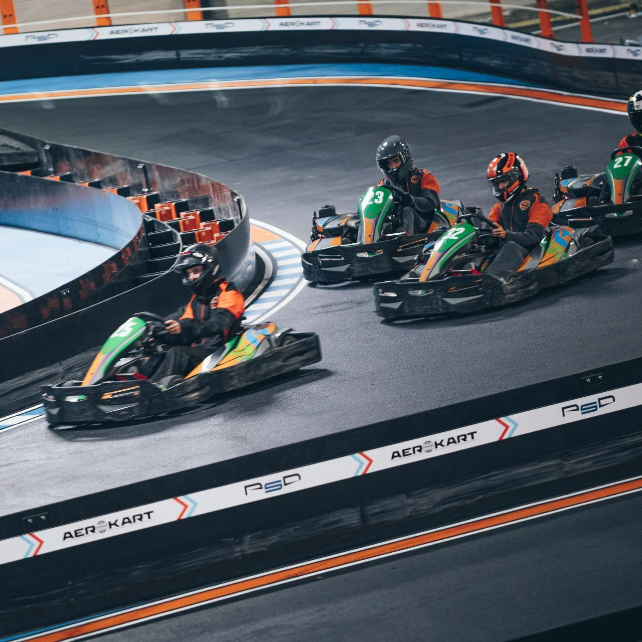 Course de karts sur une piste intérieure, les pilotes portant des casques et des combinaisons de course.