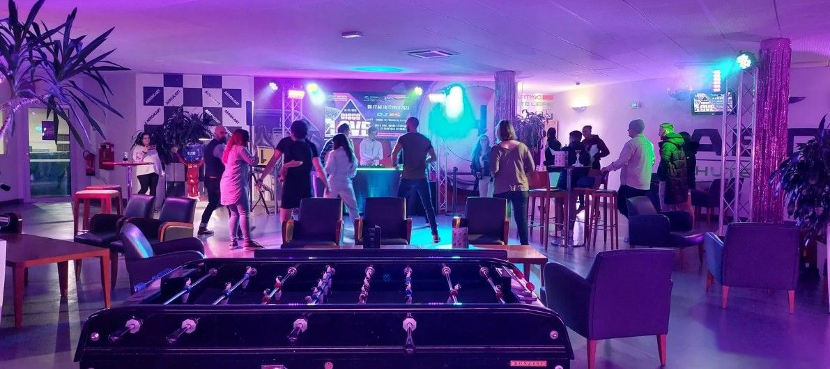 Un groupe se produit sur scène dans une salle avec un baby-foot au premier plan. Éclairage violet.