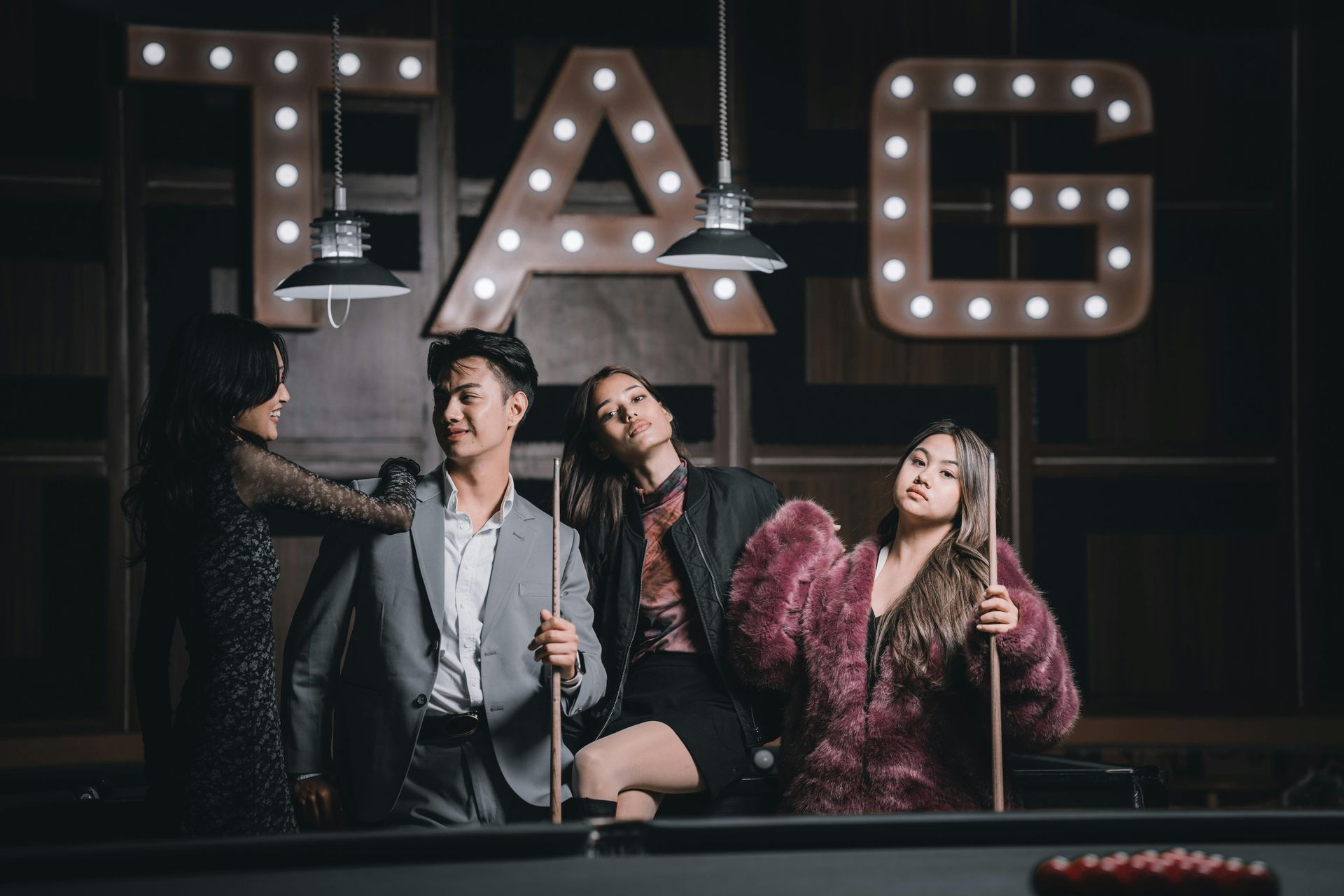Quatre personnes posent autour d'une table de billard sous une enseigne « TAG ». Éclairage tamisé et feutré.