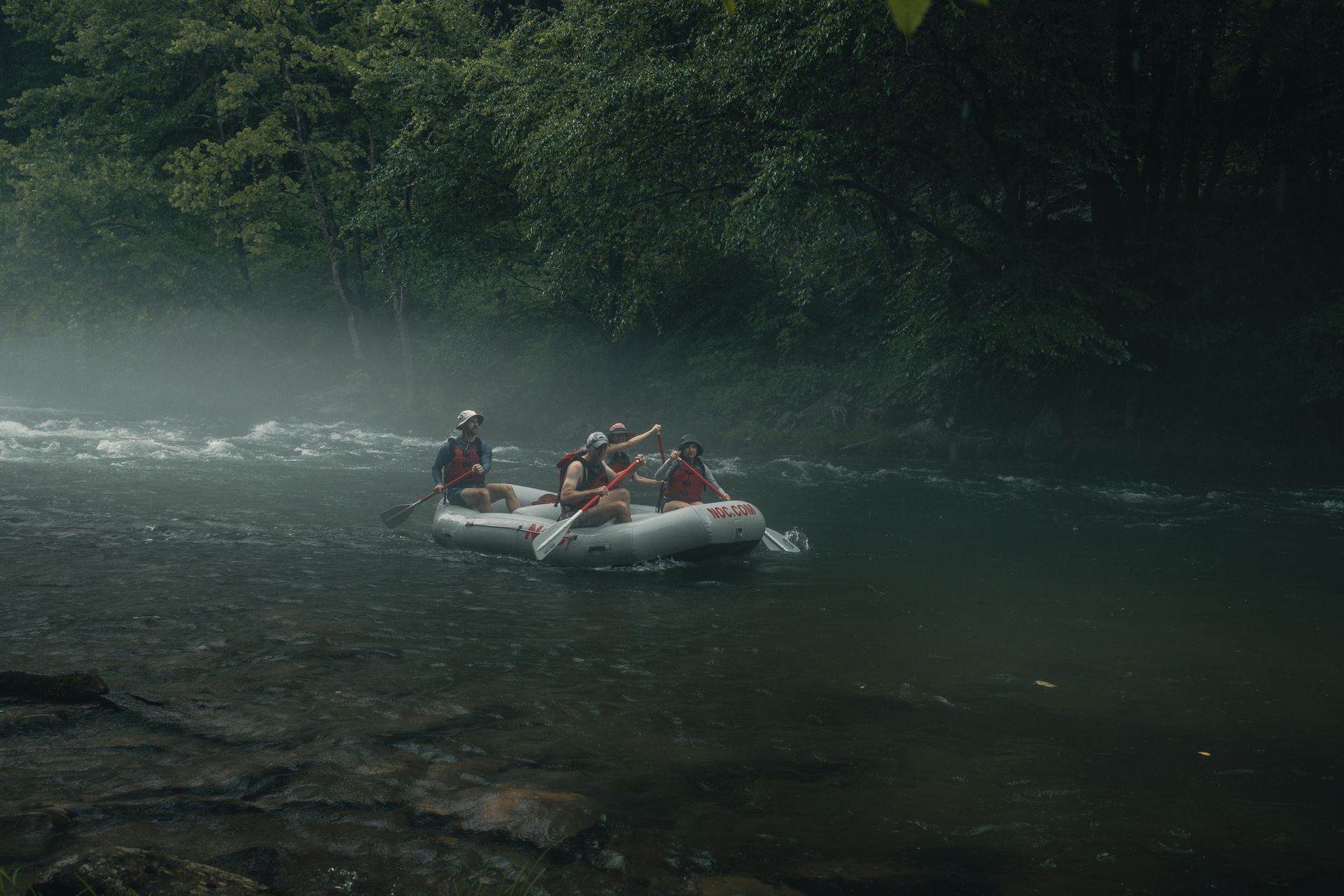 Descente en rafting sur une rivière brumeuse ; des personnes pagayent. Forêt en arrière-plan.