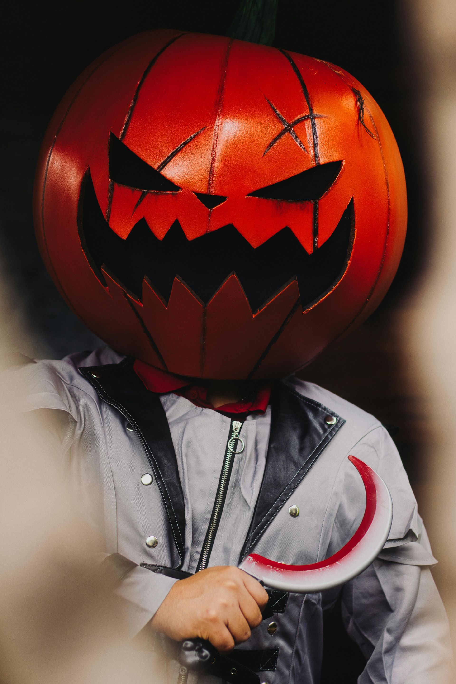 Une personne déguisée en citrouille d'Halloween tient une lame courbe. Le costume est gris et noir.