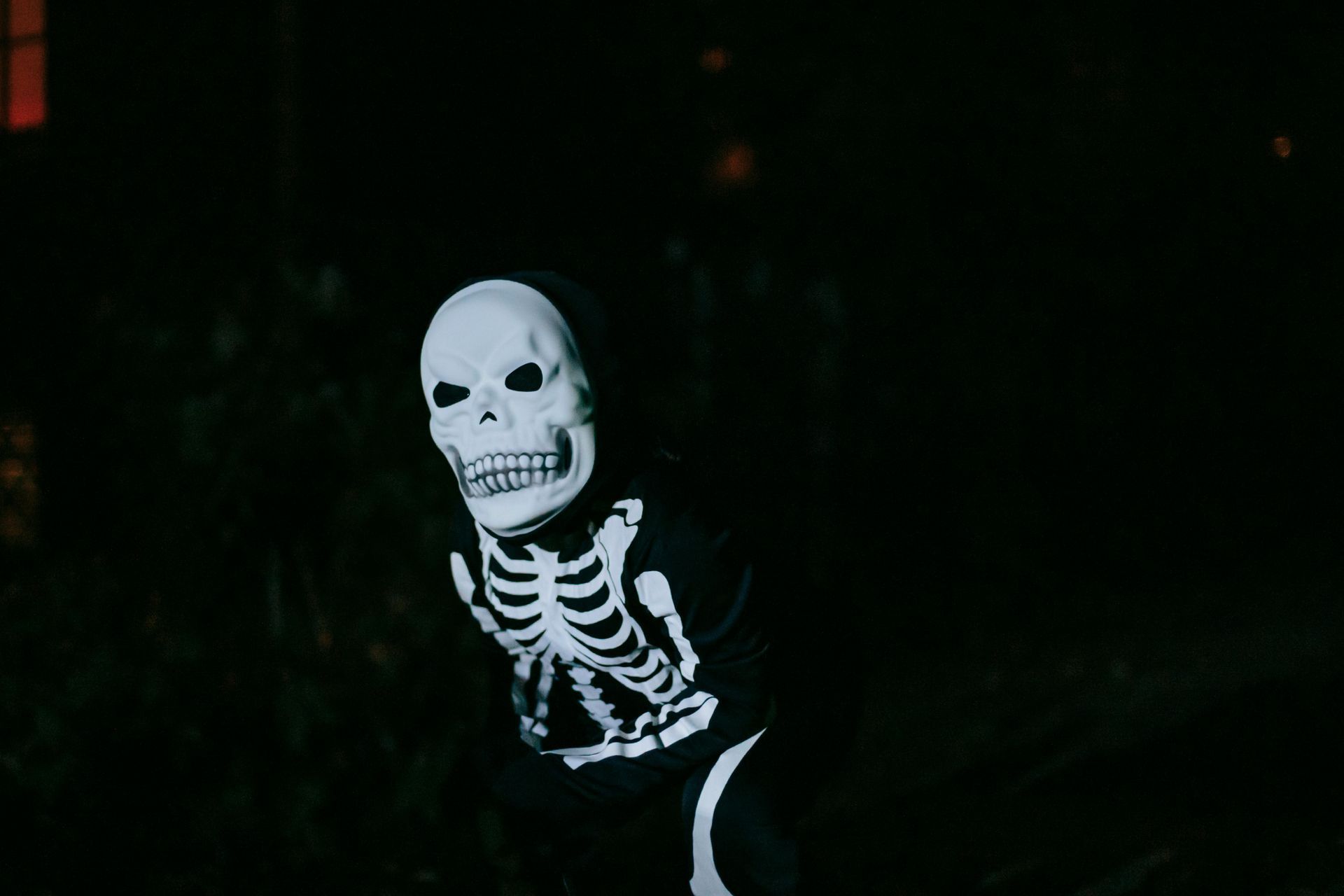 Une personne déguisée en squelette se tient dans un décor extérieur sombre.