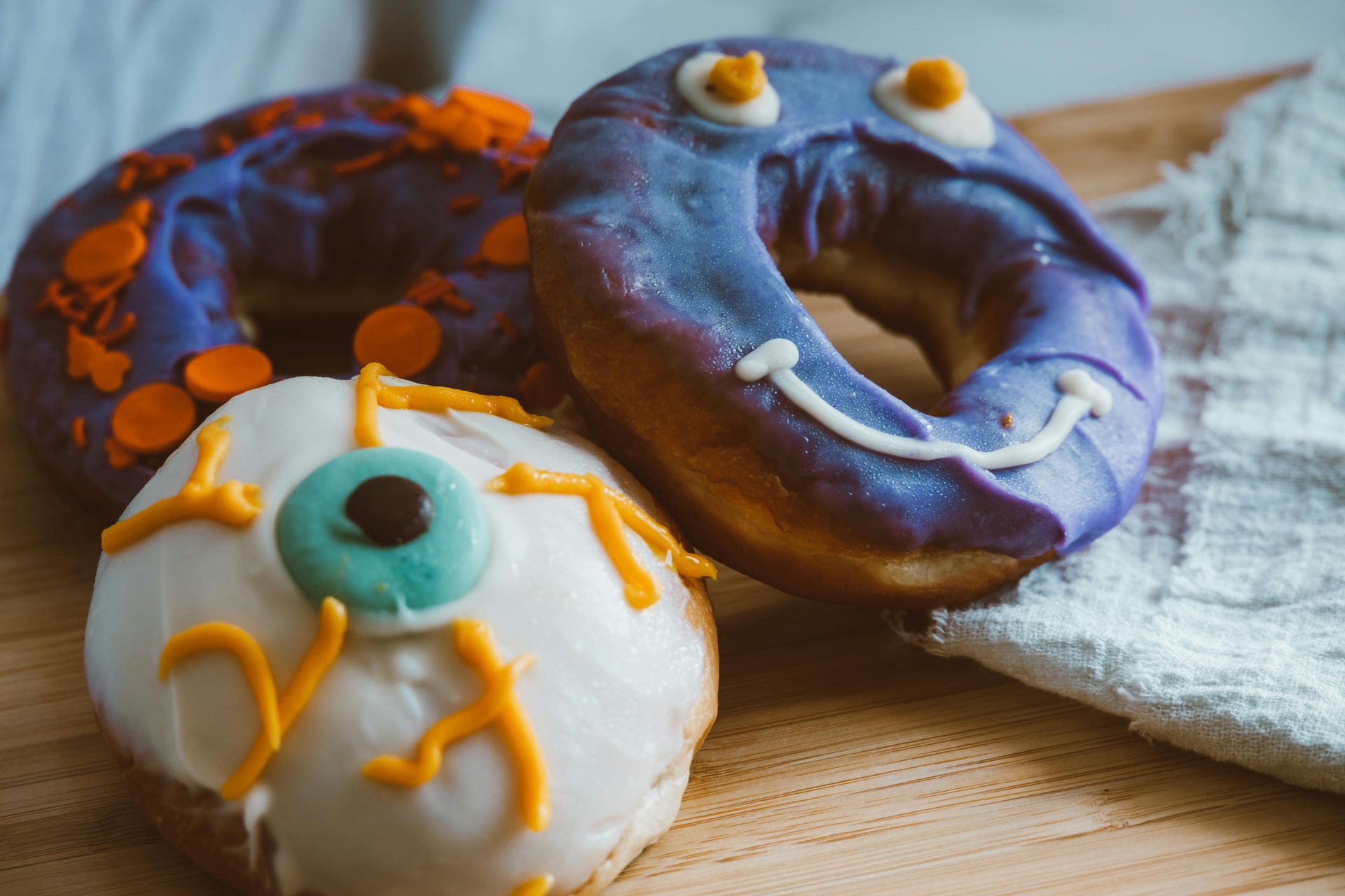 Trois beignets d'Halloween : glaçage violet avec des vermicelles orange et des visages de monstres. Beignet en forme d'œil.