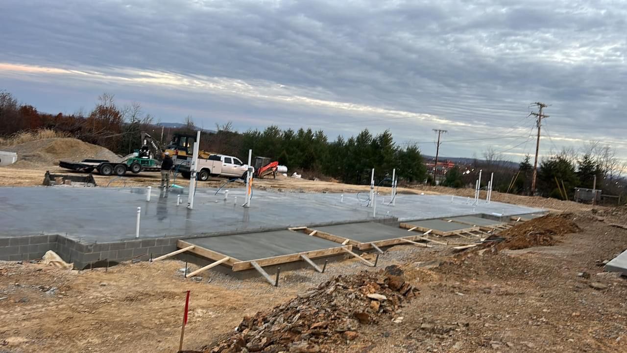 Concrete foundation slab under construction with rebar, wooden forms, and workers in the background