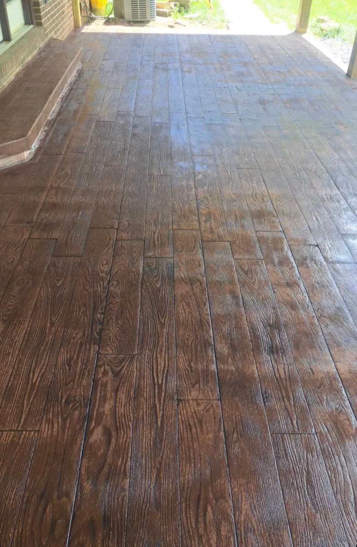 Wet wooden deck under a covered porch with sunlight at the far end