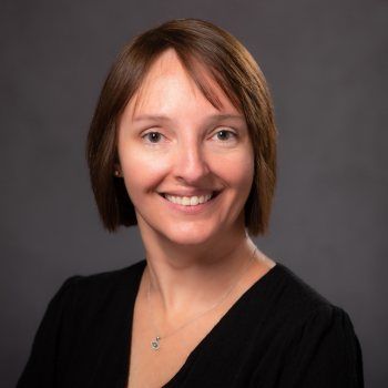 Dr. Lindsay Florkey with short brown hair, smiling, wearing a black top against a grey backdrop.