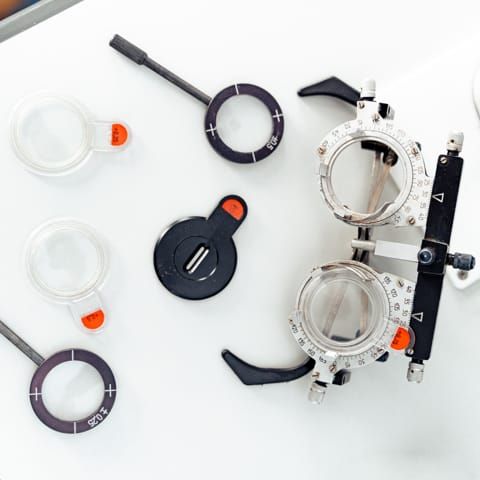 Eye exam tools, including trial lenses and a phoropter, are arranged on a white surface.