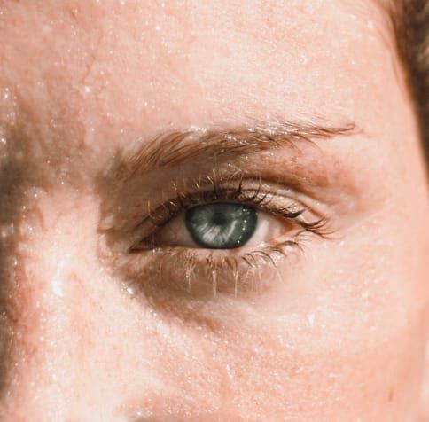 Close-up of a blue eye, wet skin, sweat droplets, eyebrow visible.
