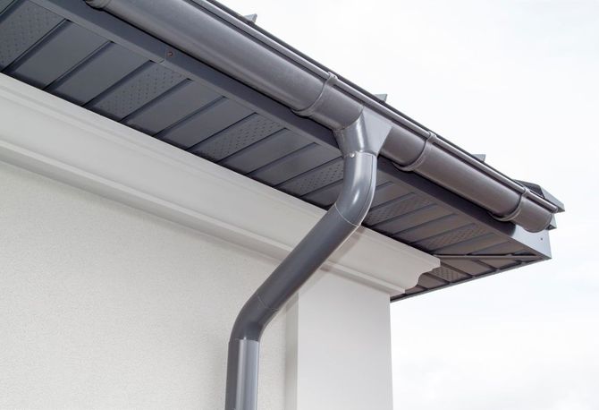 Gray rain gutter and downspout on a white house roof eave