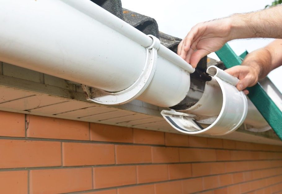 Hands using a tool to repair a white rain gutter on a brick wall