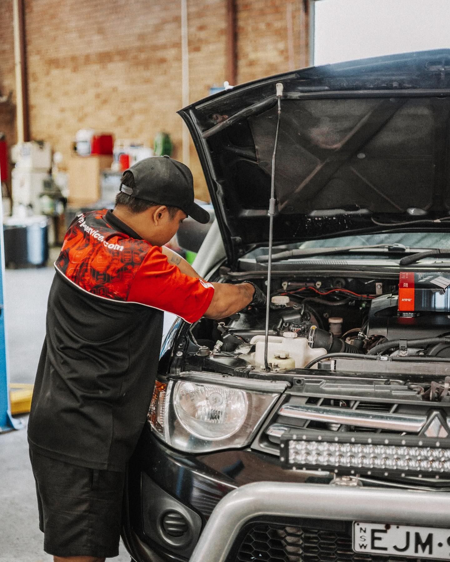Mechanic in Red Shirt Working Under a Vehicle With Arms Raised — Nationwide Auto Service Centre in West Gosford, NSW