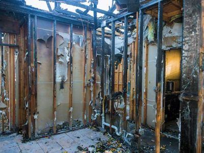 Interior of a fire-damaged room with exposed studs, charred walls, and debris on the floor.