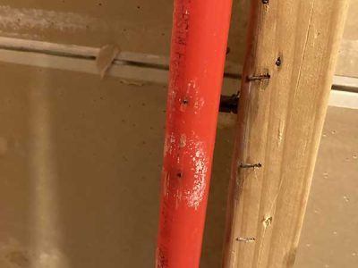 A red pipe is attached to a wooden post.