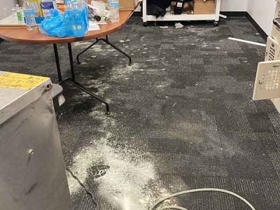 A messy room with a table and a trash can on the floor.