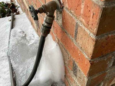 A hose is attached to a brick wall in the snow.