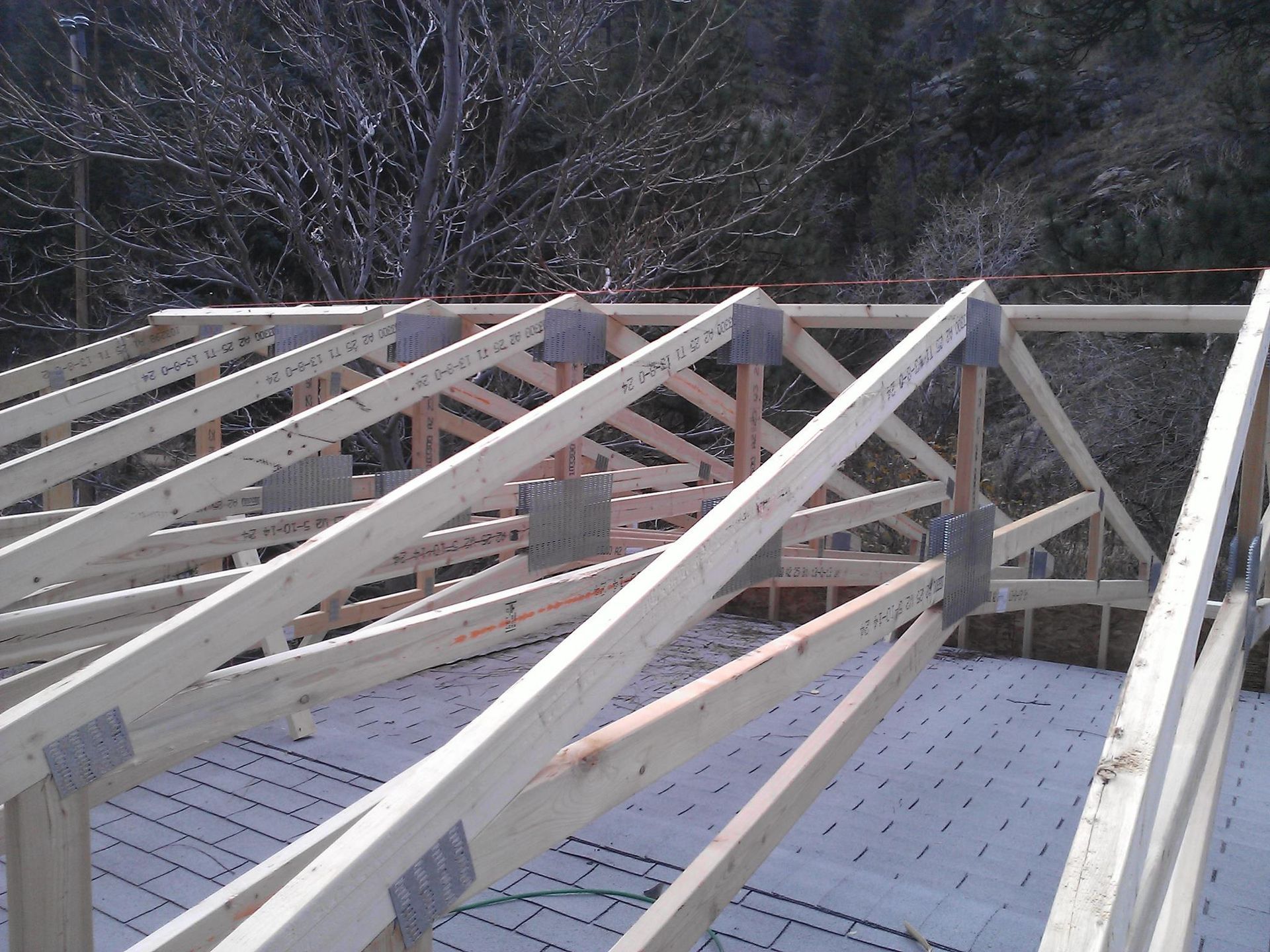 Wooden roof trusses under construction on a deck, with trees in the background.
