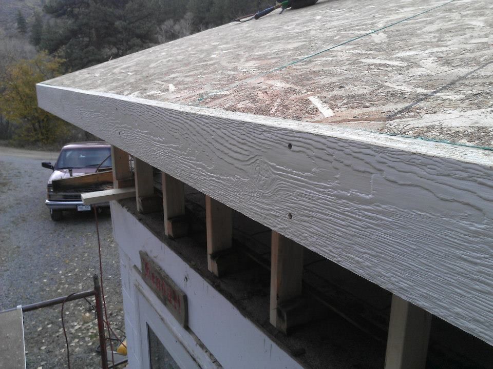 Weathered roof edge on a building, with a parked pickup truck below in a wooded area.