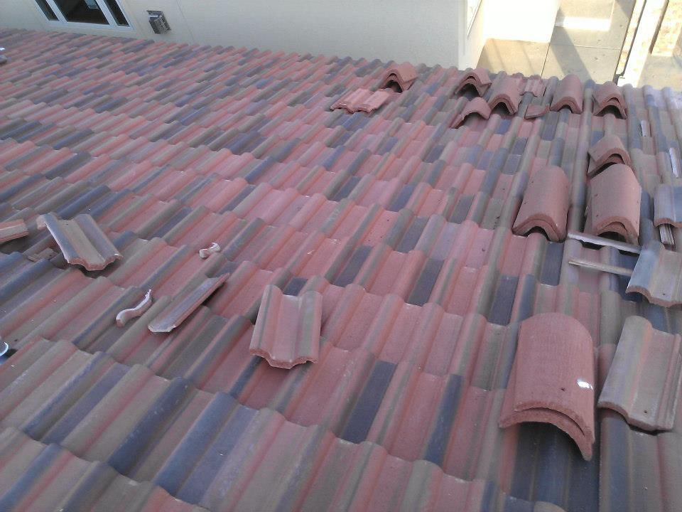Damaged red-tiled roof with several displaced tiles near the ridge and edges