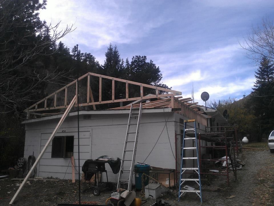 House roof under construction with ladders, lumber framing, and tools in a yard