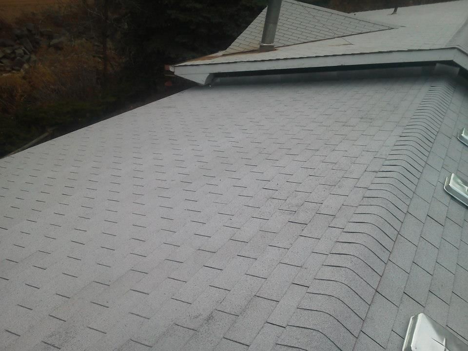 Close-up of a gray shingled roof with a sloped ridge and skylight in the background