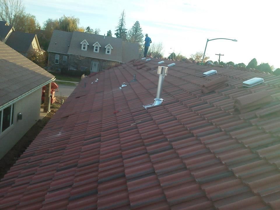 Rooftop view of a red-tiled house with vents and chimneys, neighboring homes visible at sunset.