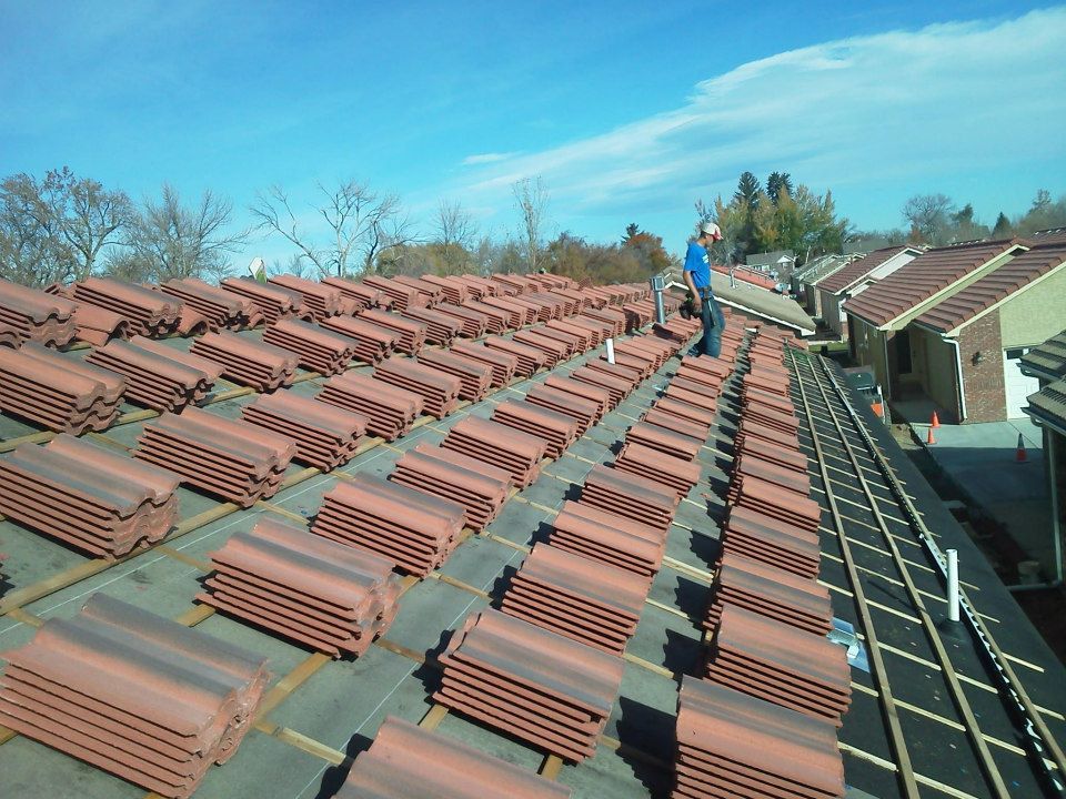 Worker inspecting rows of red roof tiles on a rooftop under a clear blue sky