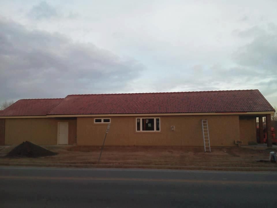 Single-story beige building with a red roof beside a road at dusk.