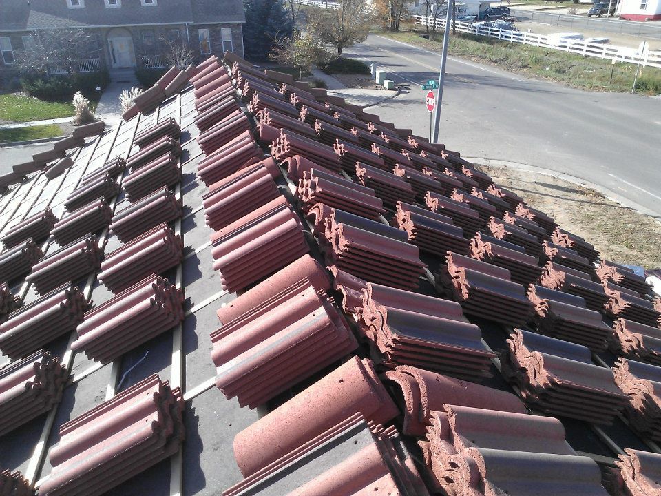 Stacked red roof tiles on a rooftop beside a road and houses on a sunny day