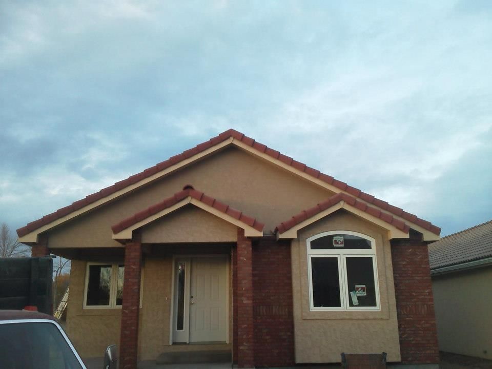 Single-story tan house with red trim, brick columns, and a front porch under a cloudy sky