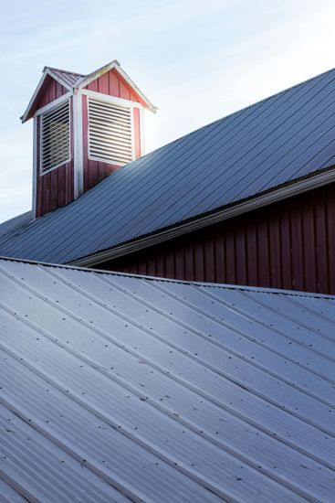 Snow-covered red barn roof with a small cupola against a pale sky
