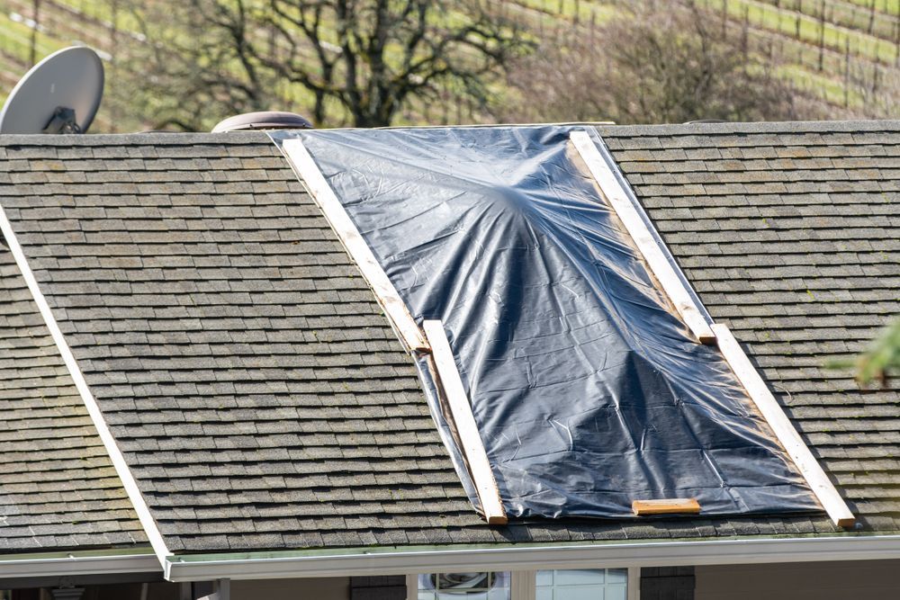 Damaged tarp-covered roof window on a shingled house roof