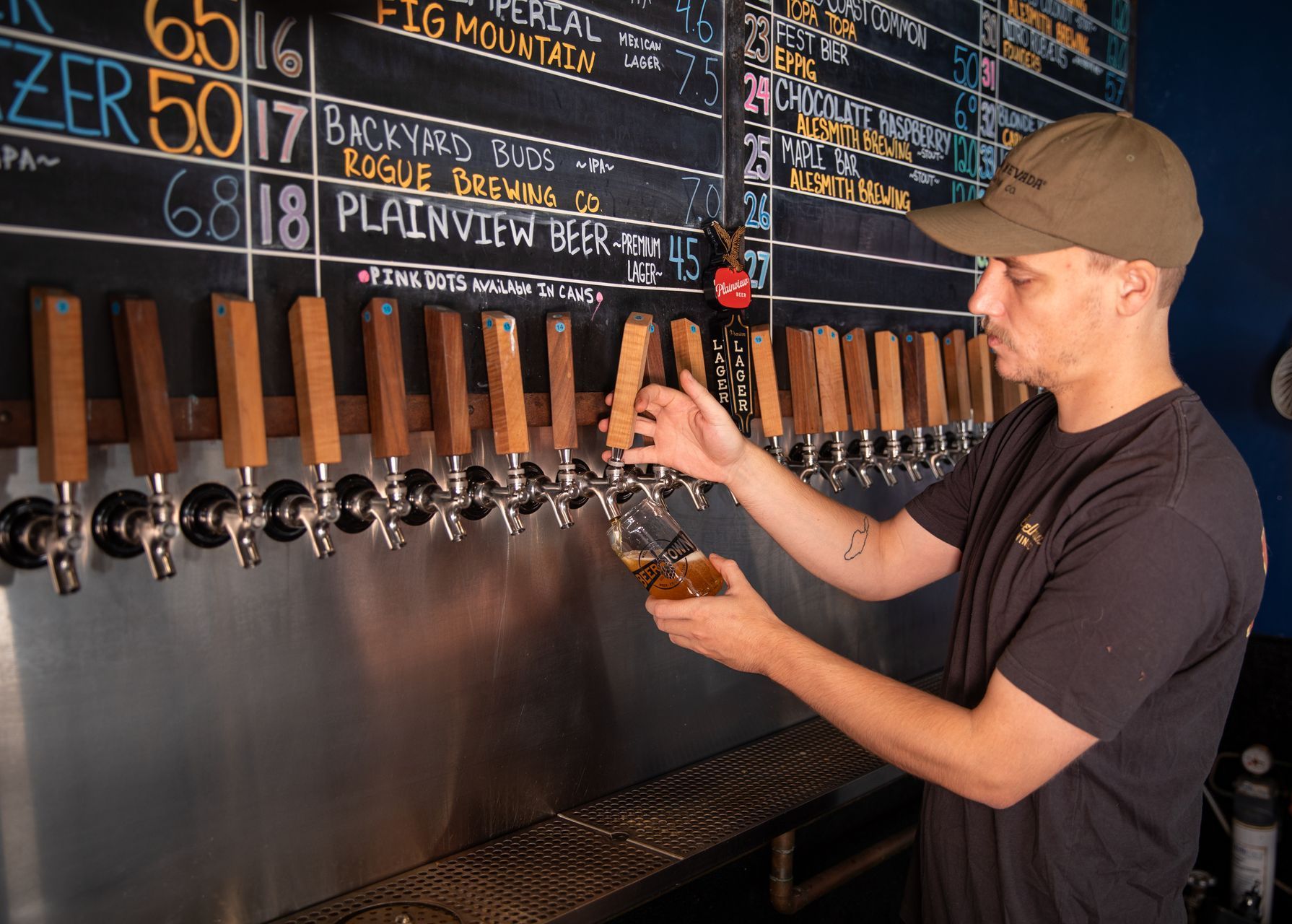 A man is pouring beer from a tap in front of a chalkboard.