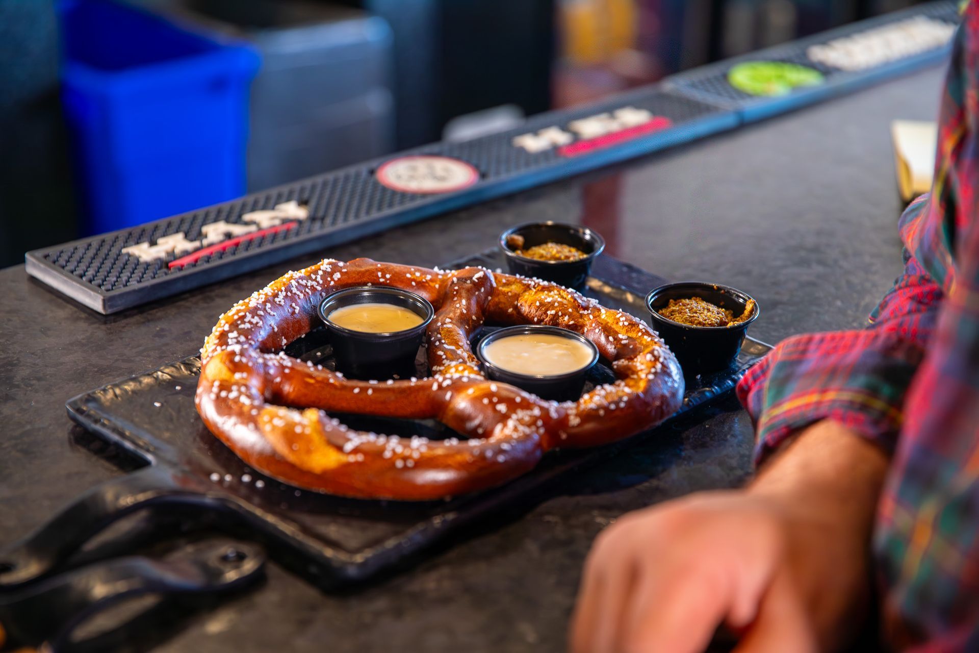A pretzel with dipping sauces on a cutting board.