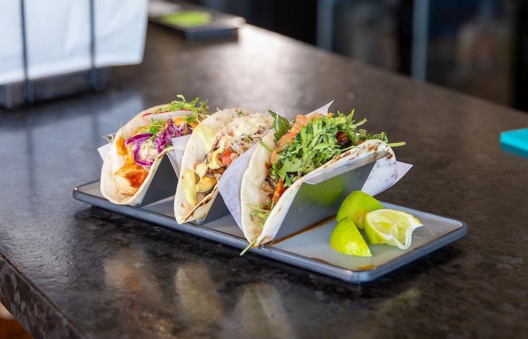 Three tacos on a plate with lime wedges on a table.