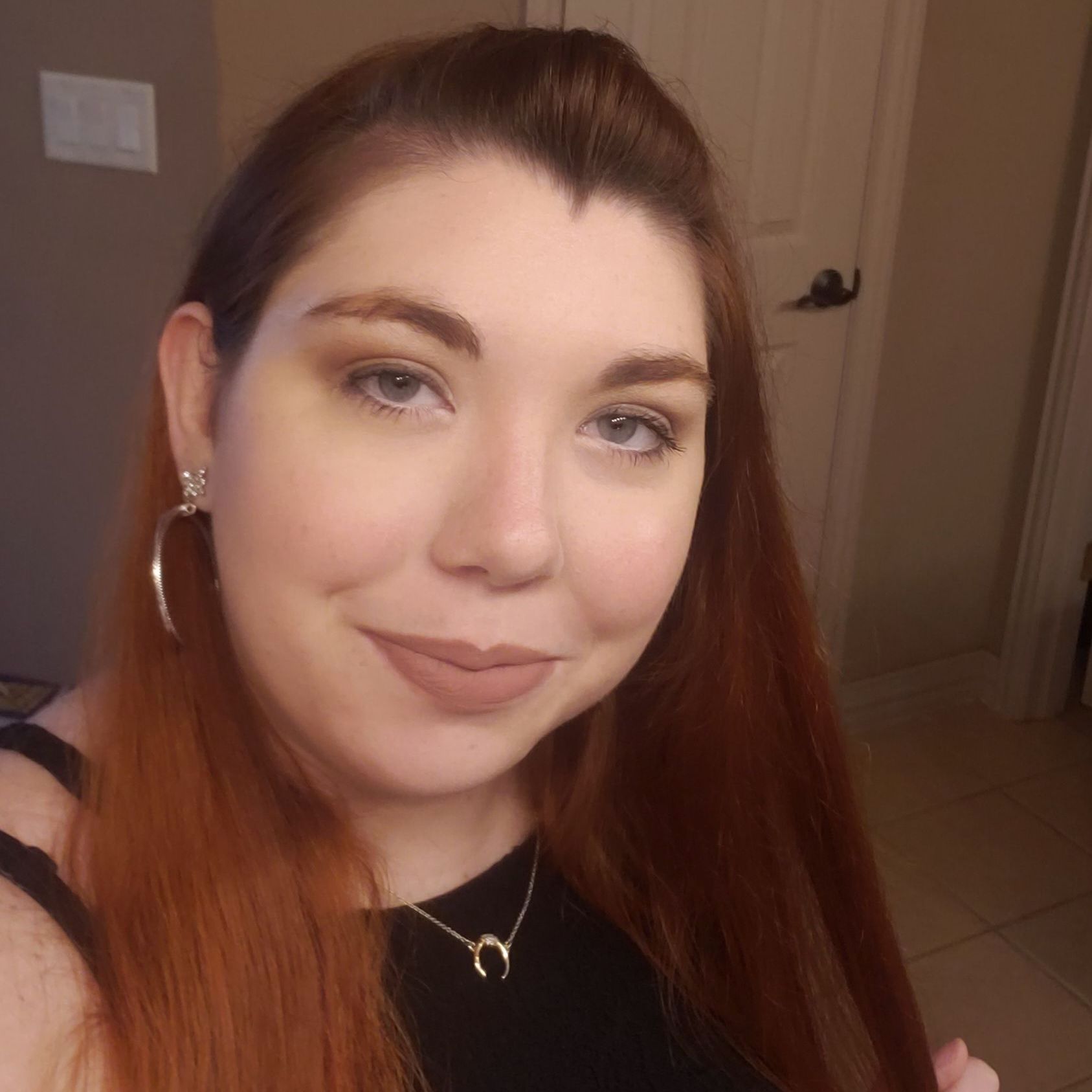 A woman with long red hair is wearing a horseshoe necklace and earrings.