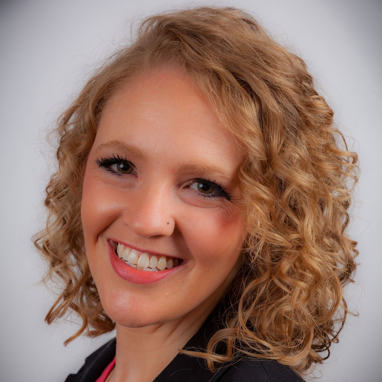 A woman with curly hair and a nose ring smiles for the camera