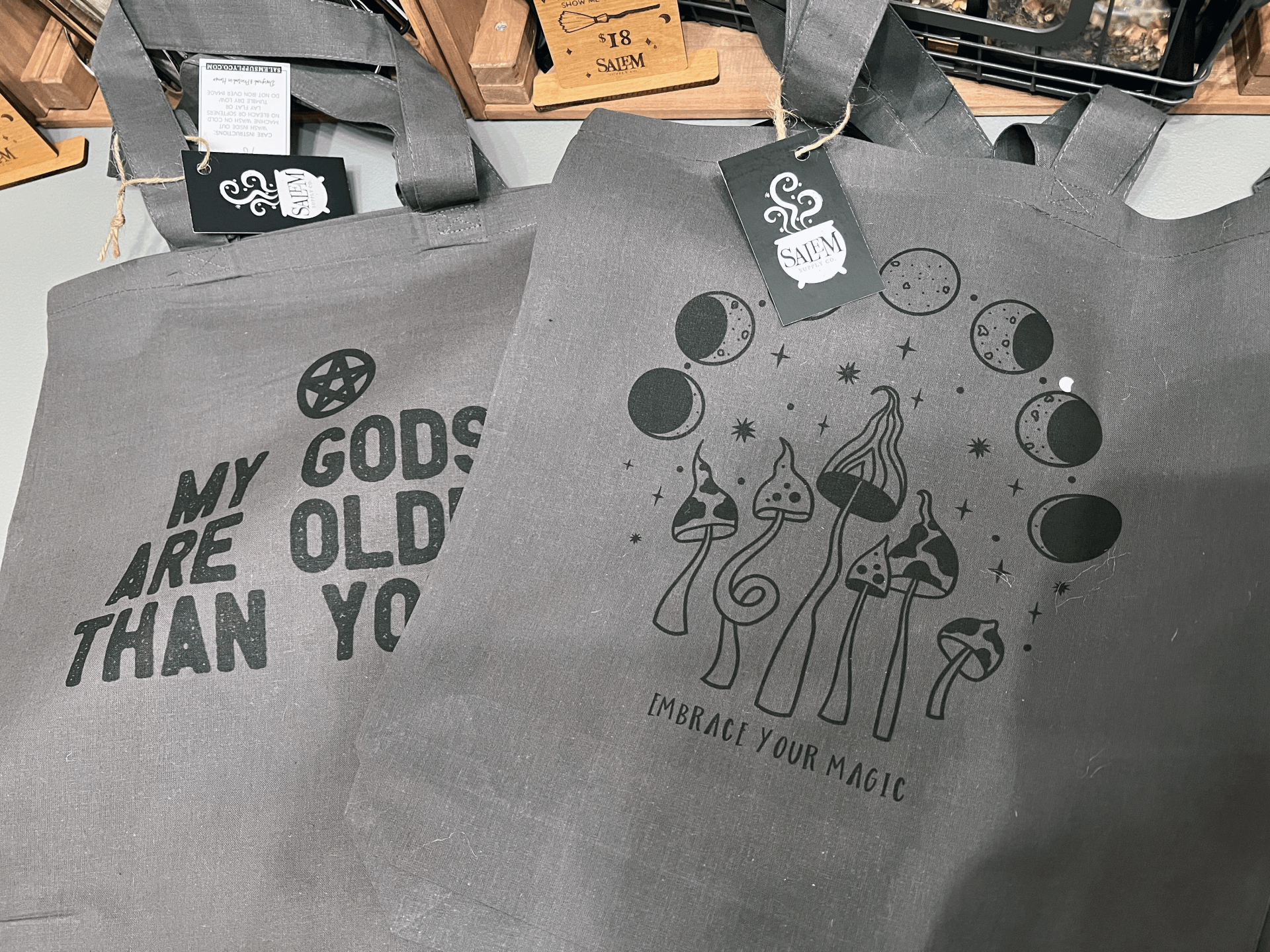Two tote bags with the words `` my gods are old than you '' on them are sitting on a table.