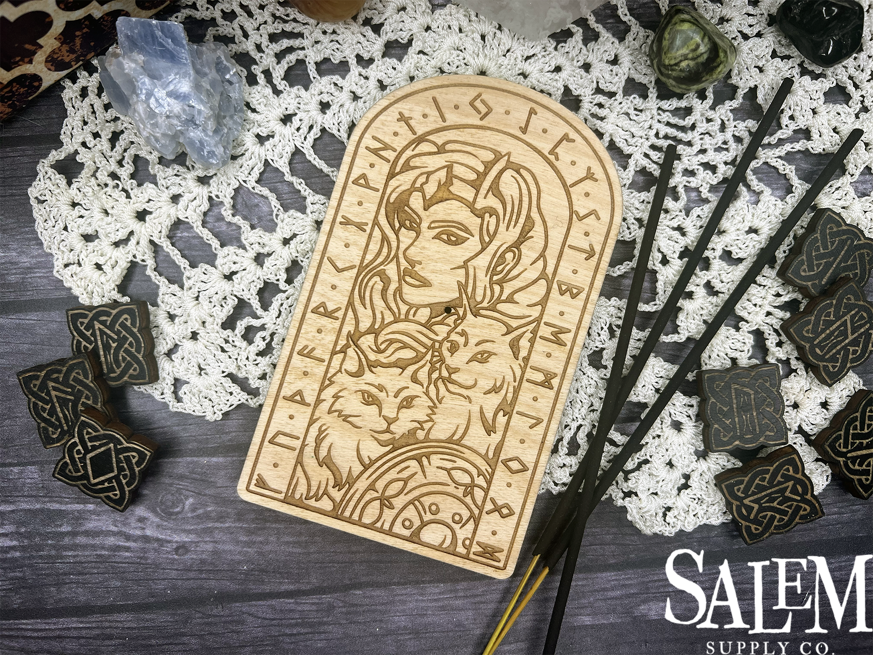 A wooden plaque with a woman and cats on it is sitting on a table next to crystals and incense sticks.